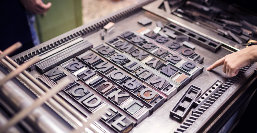 A hand pointing to large letterpress letter and number plates on a letterpress workstation.