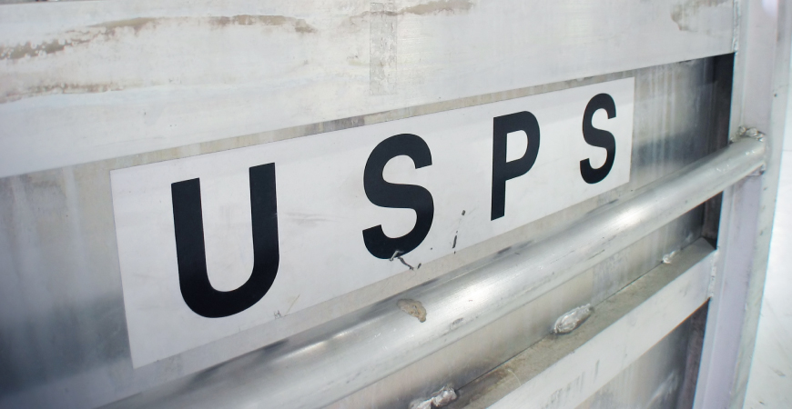 Large USPS black and white horizontal sticker on an industrial, light gray metal surface.